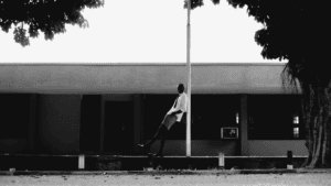 Homme introverti adossé à un poteau, posture calme et détachée, ambiance minimaliste en noir et blanc
