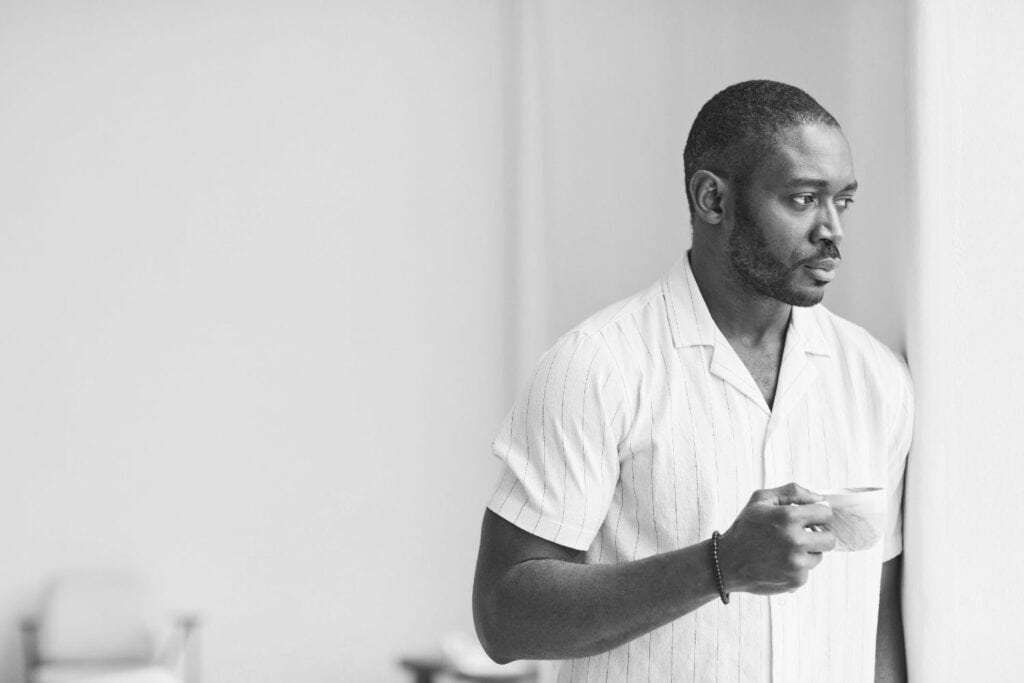 Homme debout près d’une fenêtre, tenant une tasse, plongé dans un moment de calme et de réflexion intérieure