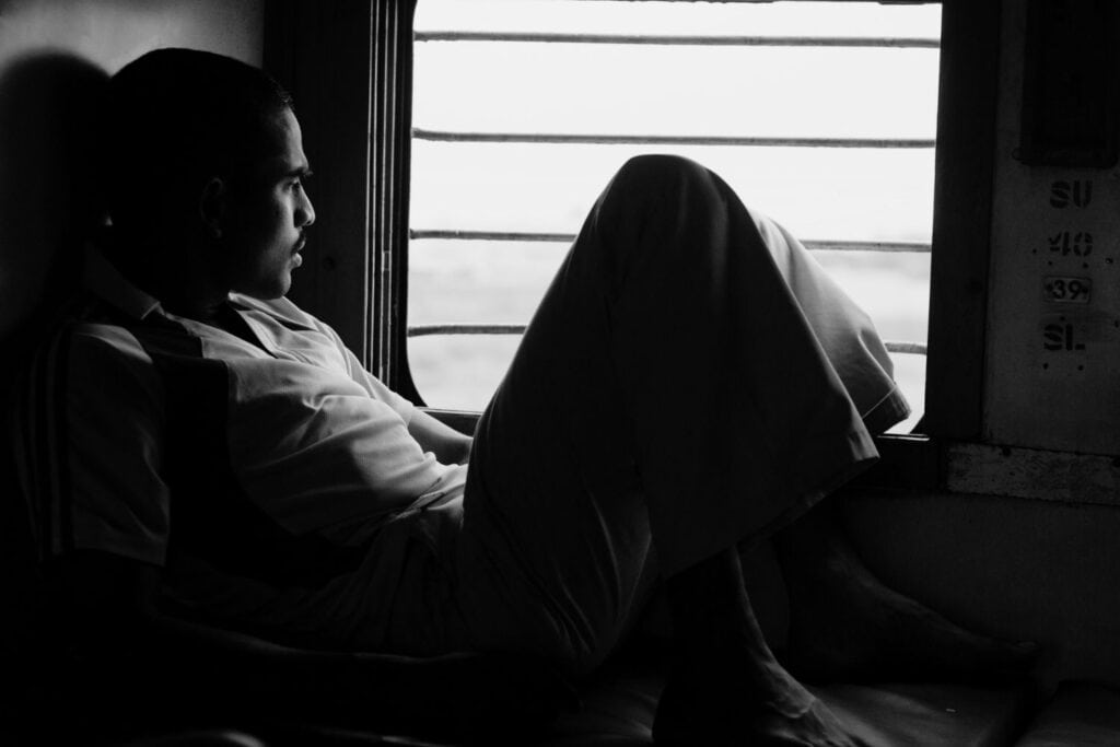 Homme assis seul dans un train, regard tourné vers la fenêtre, plongé dans une réflexion silencieuse.