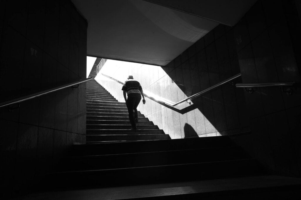Homme montant un escalier sombre vers une sortie lumineuse, symbole d’un chemin intérieur et de transformation personnelle