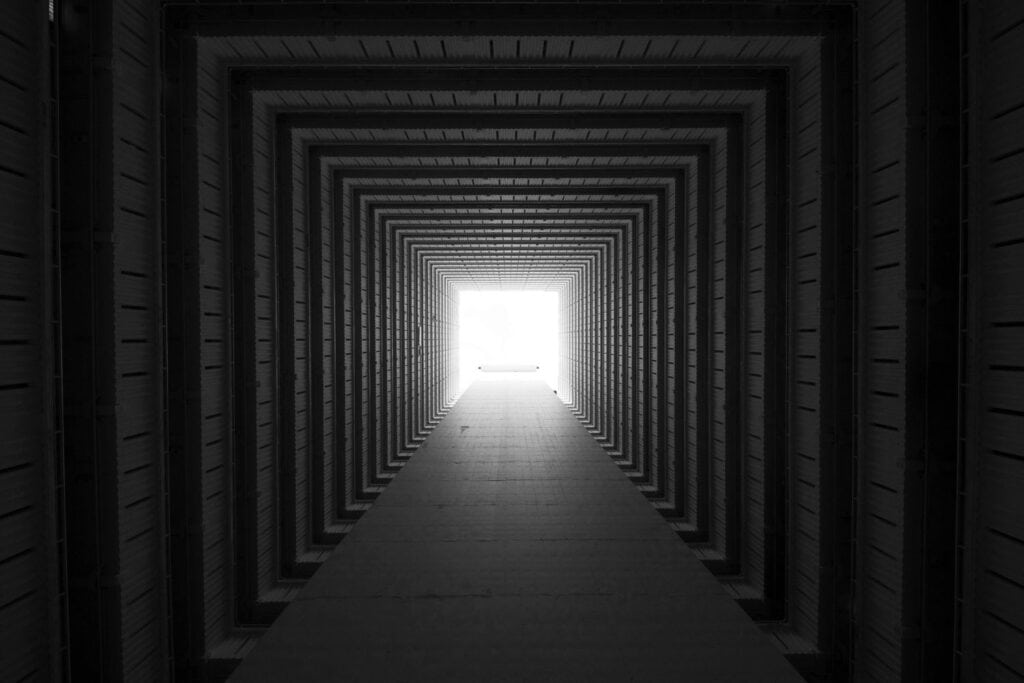 Passage architectural sombre menant vers une ouverture lumineuse, évoquant un cheminement intérieur.