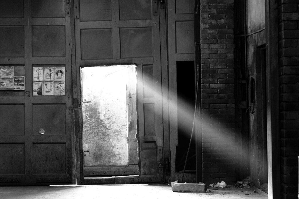 Porte entrouverte laissant passer la lumière dans un espace sombre, symbole d’un chemin personnel et non conformiste.